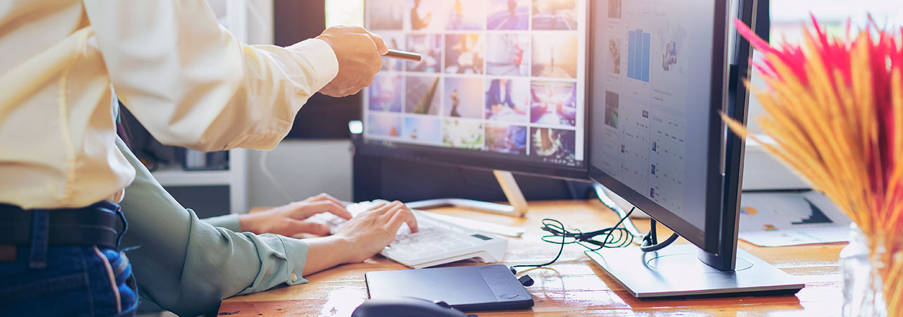 Eine Person zeigt mit einem Stift auf einen Bildschirm und andere Person schreibt auf einer Tastatur